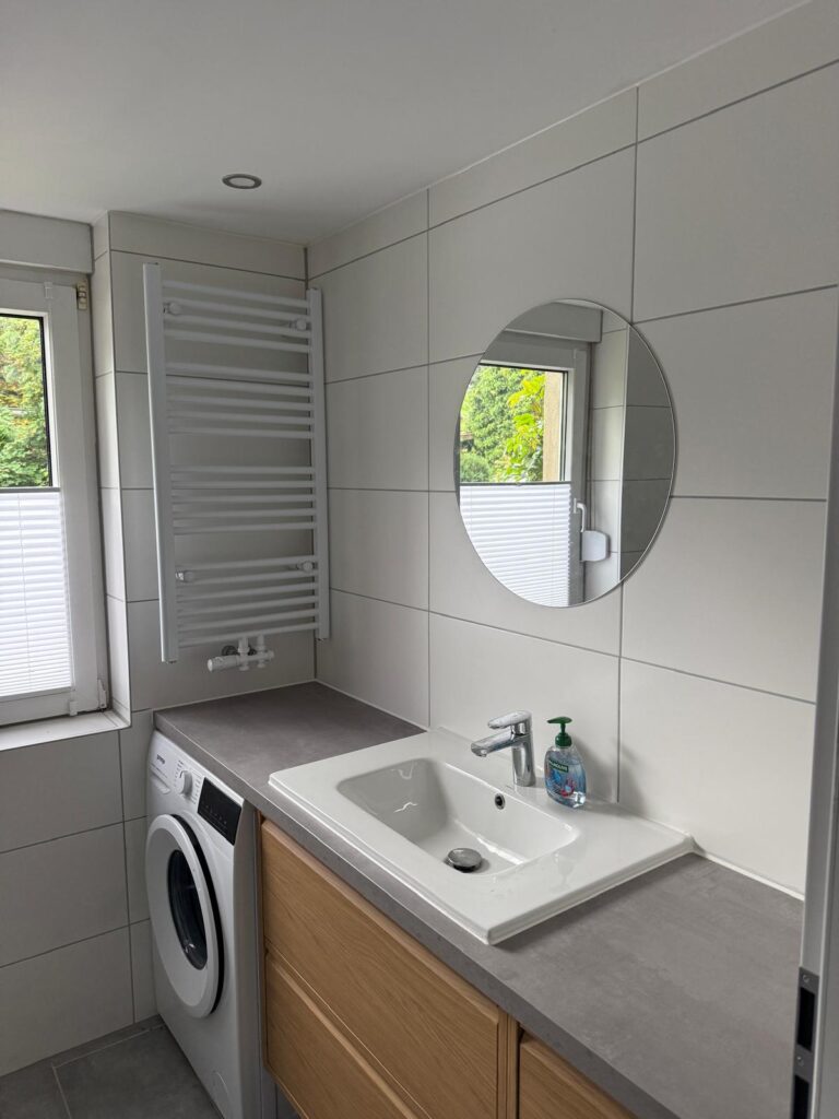 Badezimmer mit Waschtisch, rundem Spiegel und Waschmaschine