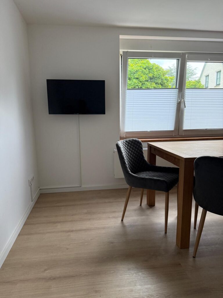 Essbereich der Ferienwohnung mit Holztisch, gepolsterten Stühlen und Wand-Fernseher