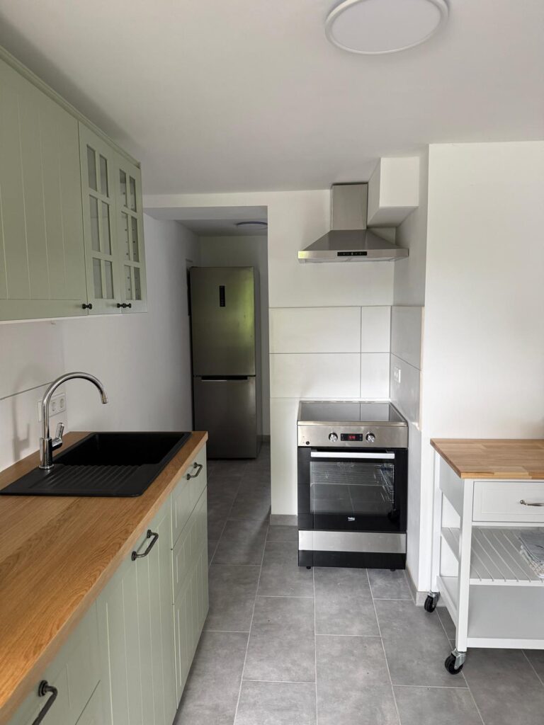 Helle Küche der Ferienwohnung Damerow mit salbeigrünen Schränken, Holzarbeitsplatte und Induktionsherd