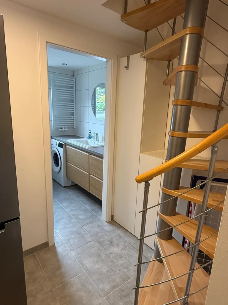 Flur der Ferienwohnung mit Wendeltreppe und Blick ins Bad mit Waschmaschine, Waschtisch und Handtuchheizkörper