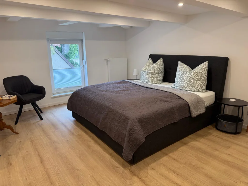 Schlafzimmer im Obergeschoss der Ferienwohnung mit Doppelbett, Sessel am Fenster und Beistelltisch