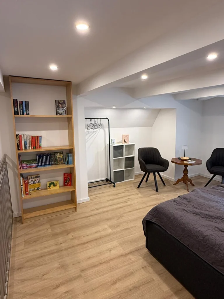 Schlafzimmer im Obergeschoss der Ferienwohnung mit Bücherregal, Kleiderstange, zwei Sesseln am Beistelltisch und Doppelbett